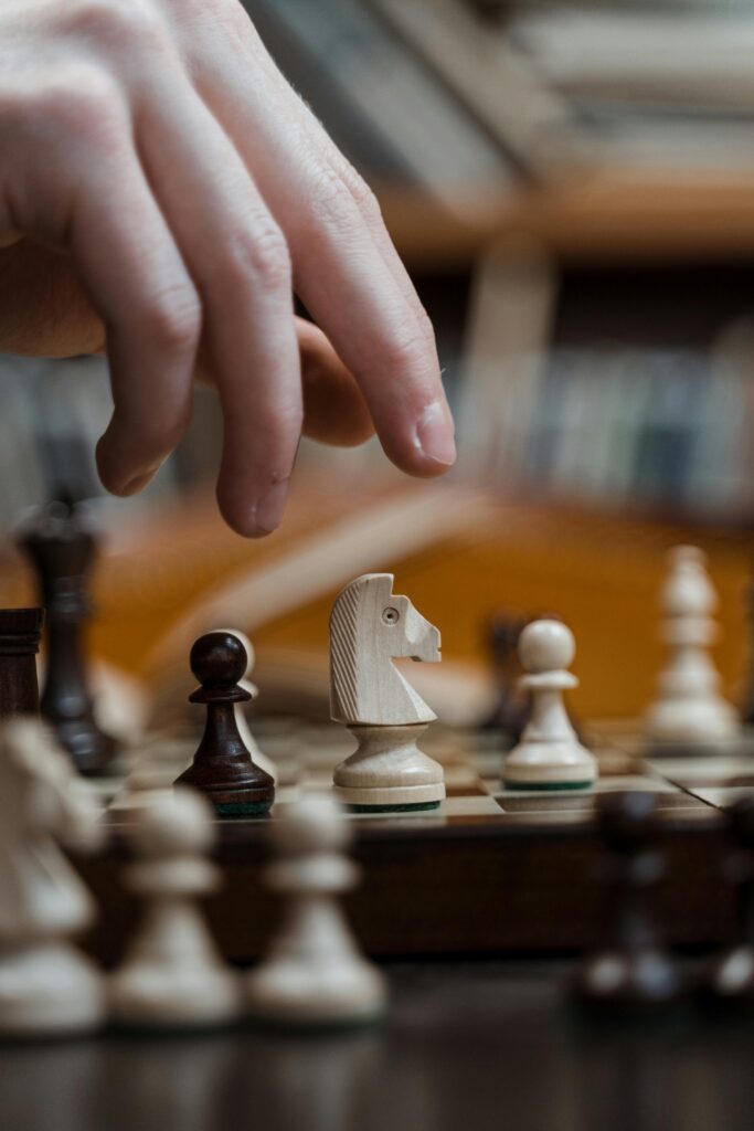 Home Hand poised over a chessboard, selecting a knight for a strategic move in a focused game.
