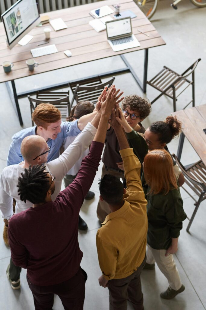 Home A diverse group of professionals high-fiving in a modern office, showcasing teamwork and collaboration.